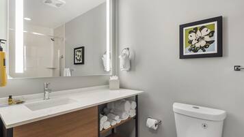 A modern bathroom with a large mirror, a sink, a toilet, and a shelf with towels.