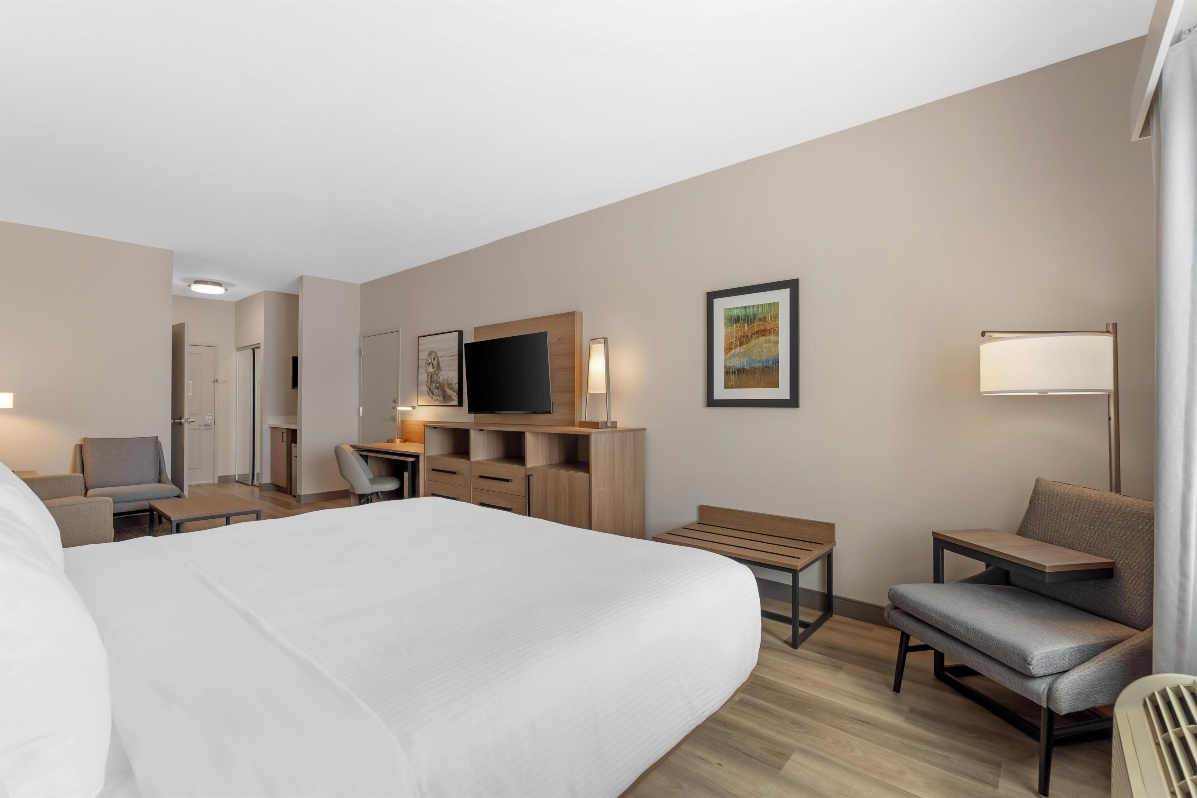 A hotel room with a large bed, a desk, a chair, a TV, and a painting on the wall.