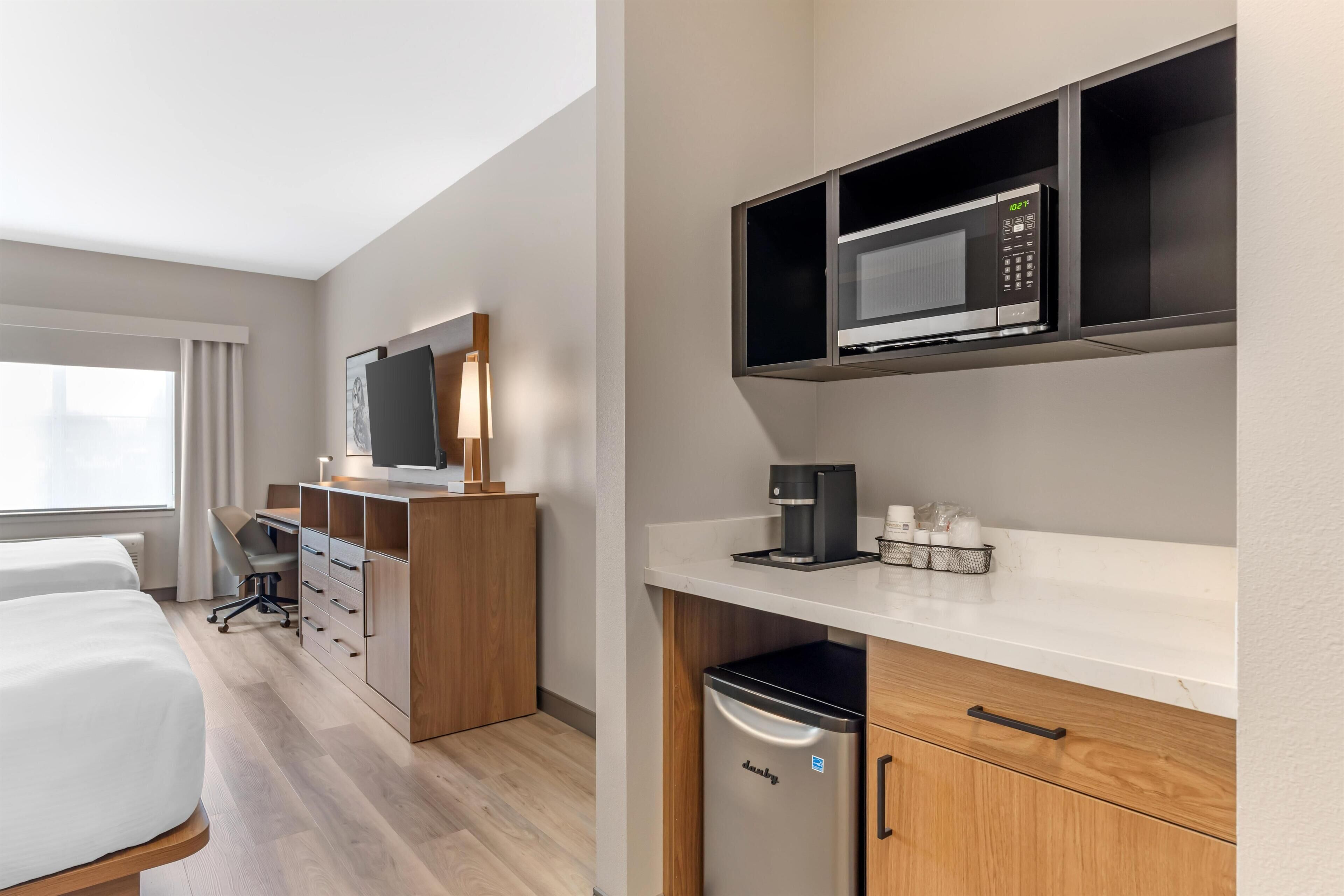 A hotel room with a bed, a desk, a television, a microwave, and a coffee machine.