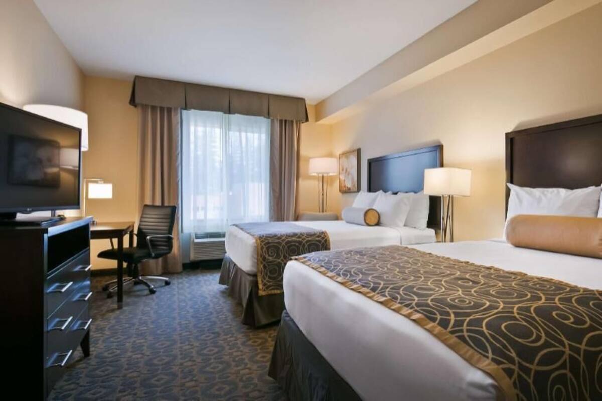 A hotel room with two beds, a desk, a TV, and a window with curtains.