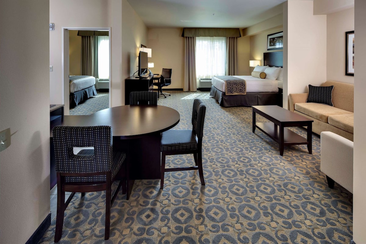 A hotel room with a bed, a desk with a chair, a sofa, and a patterned carpet.
