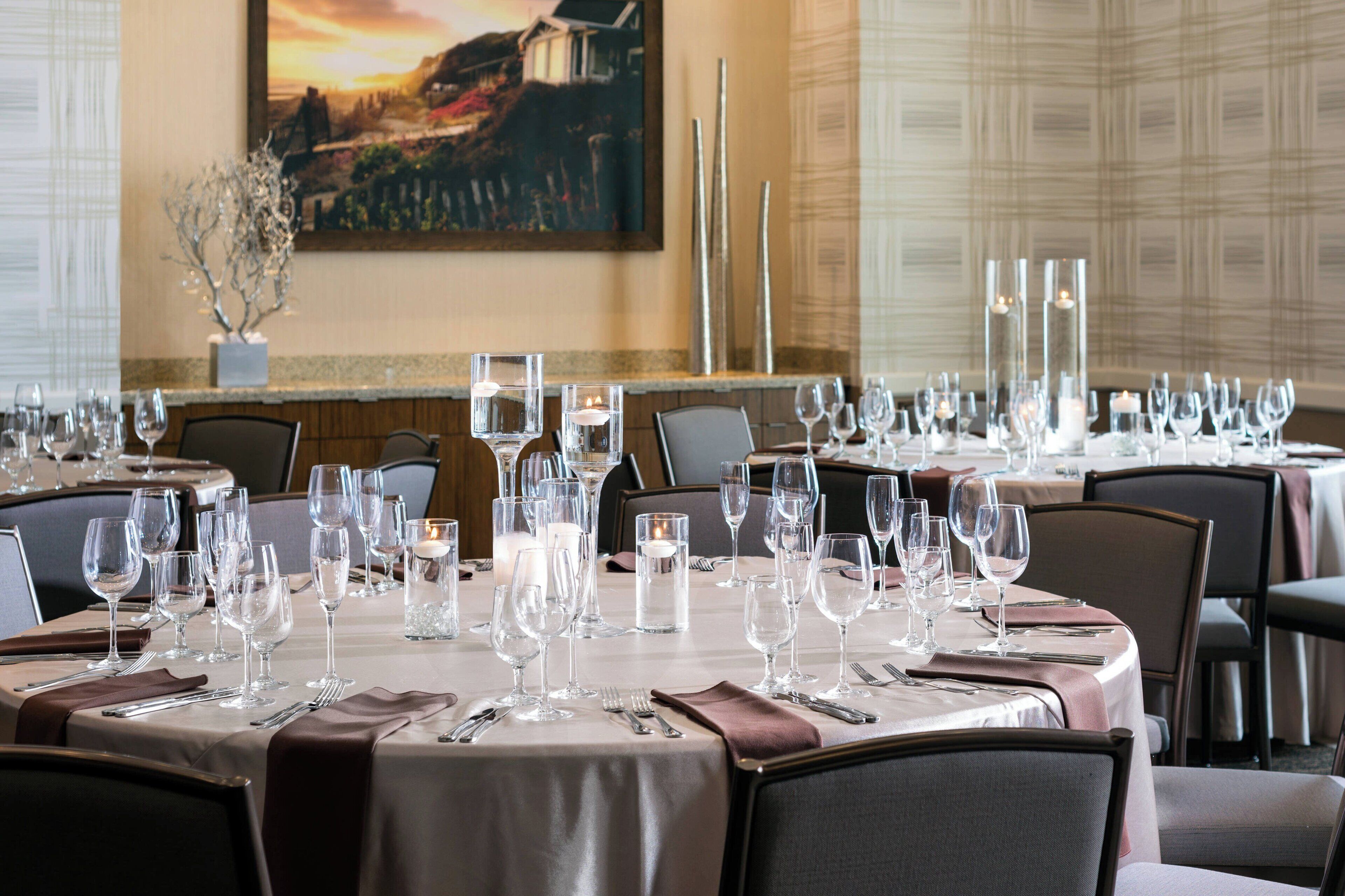 A dining area with multiple tables set for a formal meal, featuring clear glassware and candles.