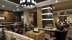 A modern lobby with a fireplace, leather chairs, a coffee table, and a reception desk.