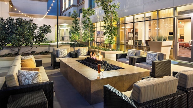An outdoor seating area with a fire pit, lounge chairs, and a view of the building's interior.