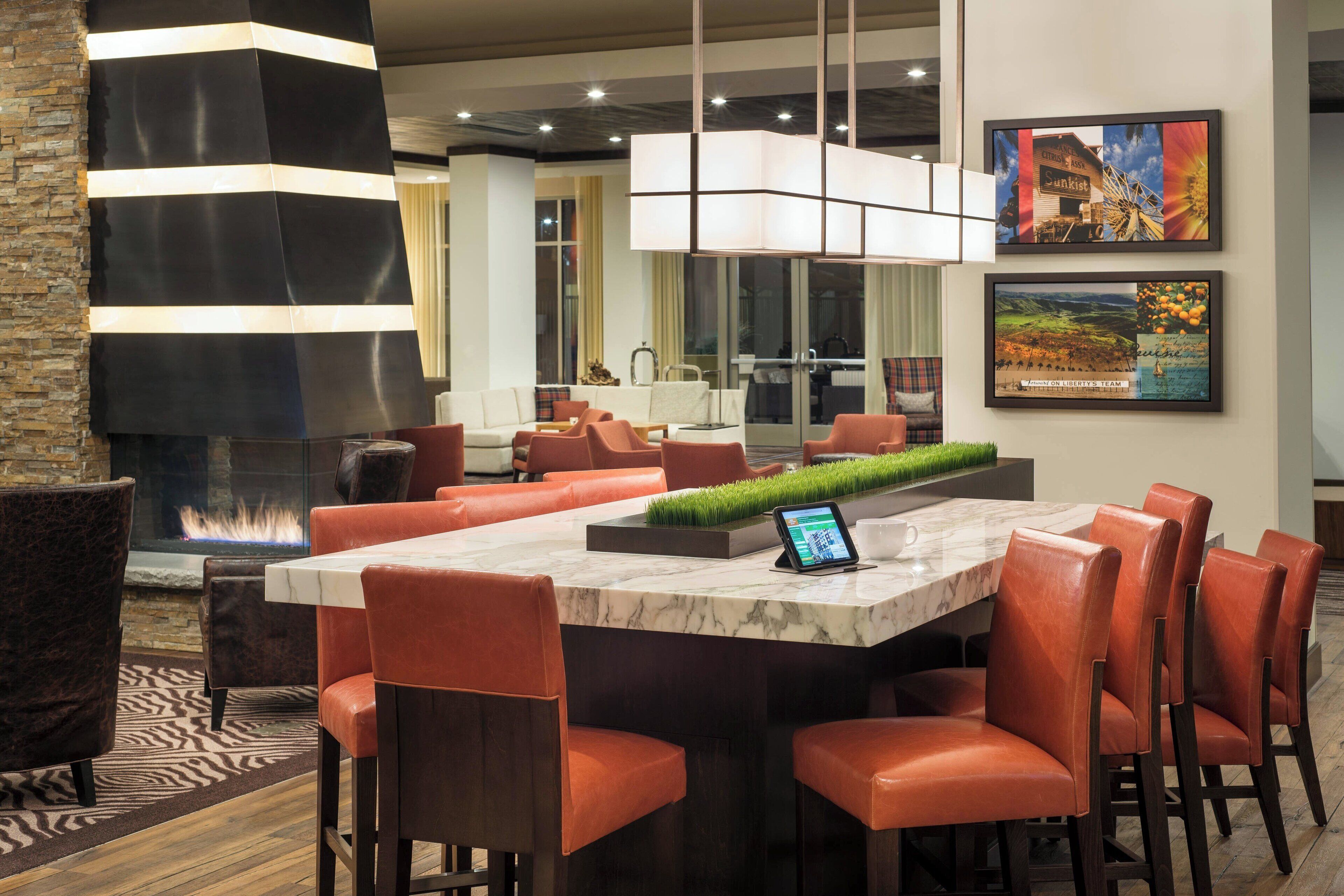 A modern dining area with a marble table, leather chairs, and a fire feature.
