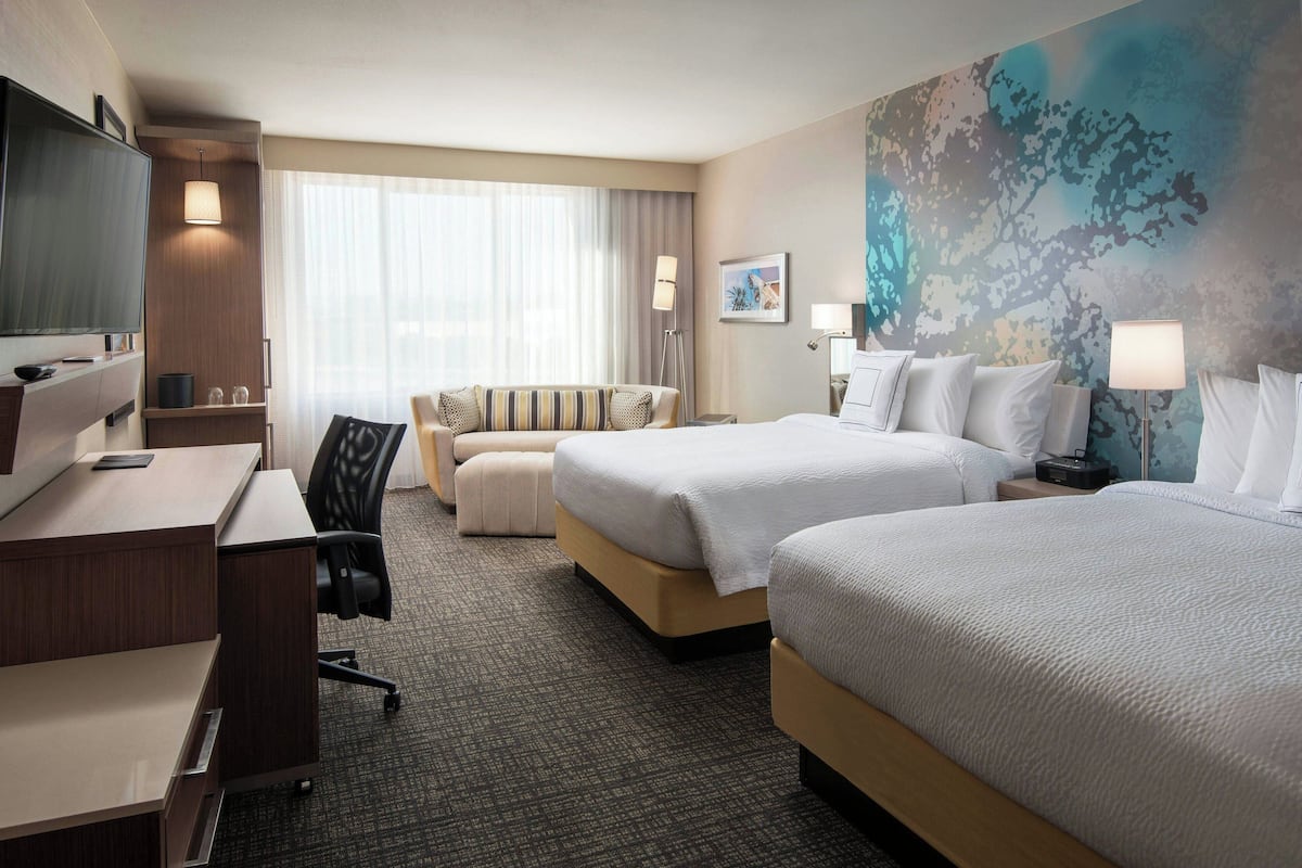 A hotel room with a bed, a desk, a chair, a TV, and a large window with curtains.