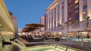 A hotel pool area with lounge chairs and umbrellas, a hot tub, and a Marriott hotel building in the background.