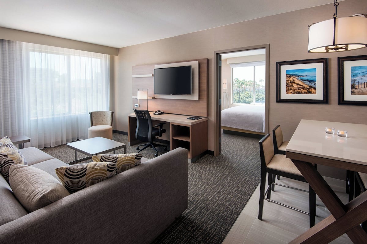 A hotel room with a sofa, a desk with a chair, a TV, and framed pictures on the wall.