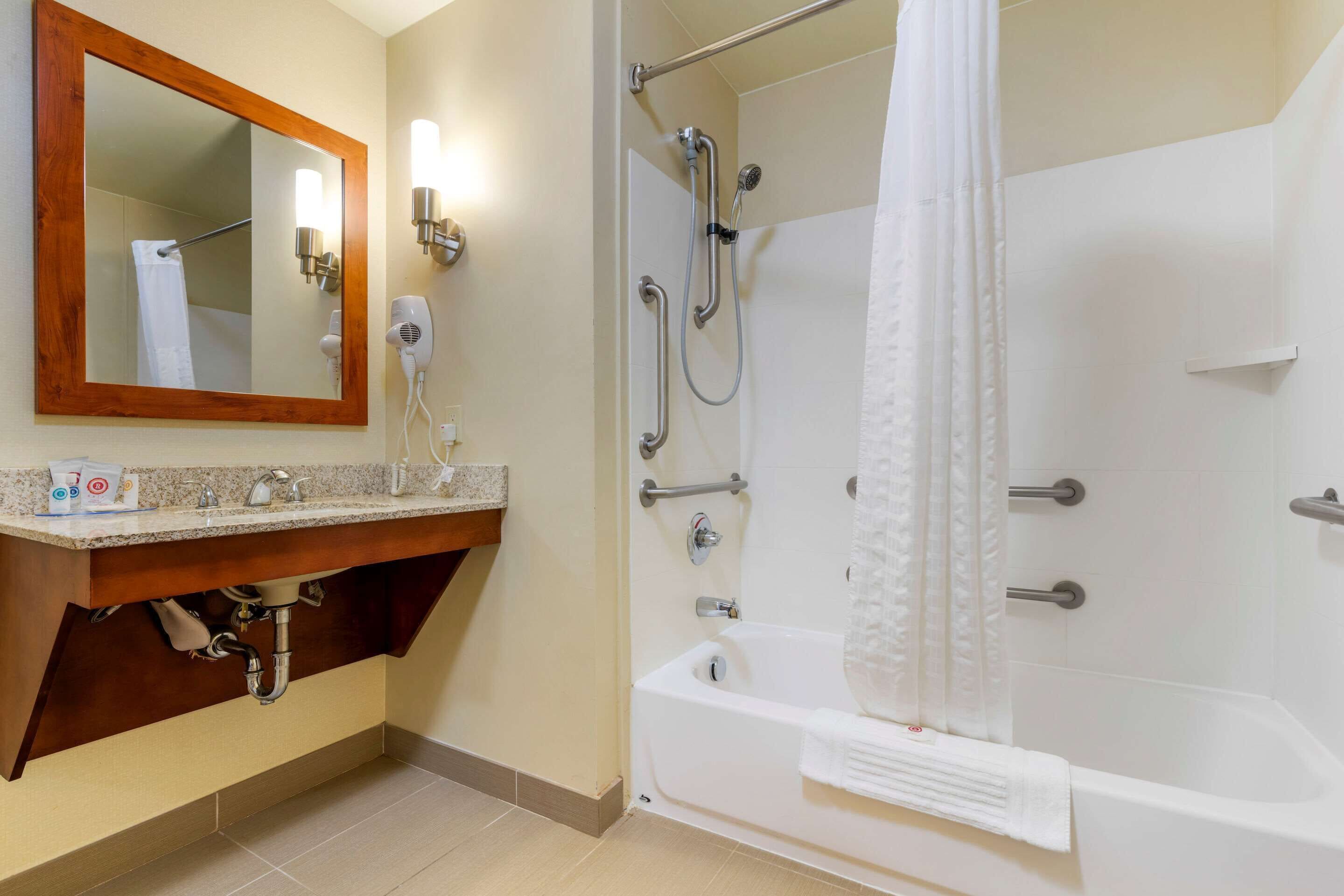 Une salle de bain avec un meuble-lavabo en bois, un grand miroir, une douche avec une porte en verre et une baignoire.