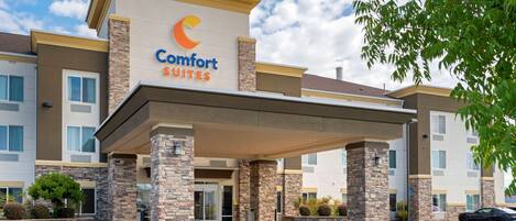 Un hotel Comfort Suites con entrada techada, pilares de piedra y estacionamiento.