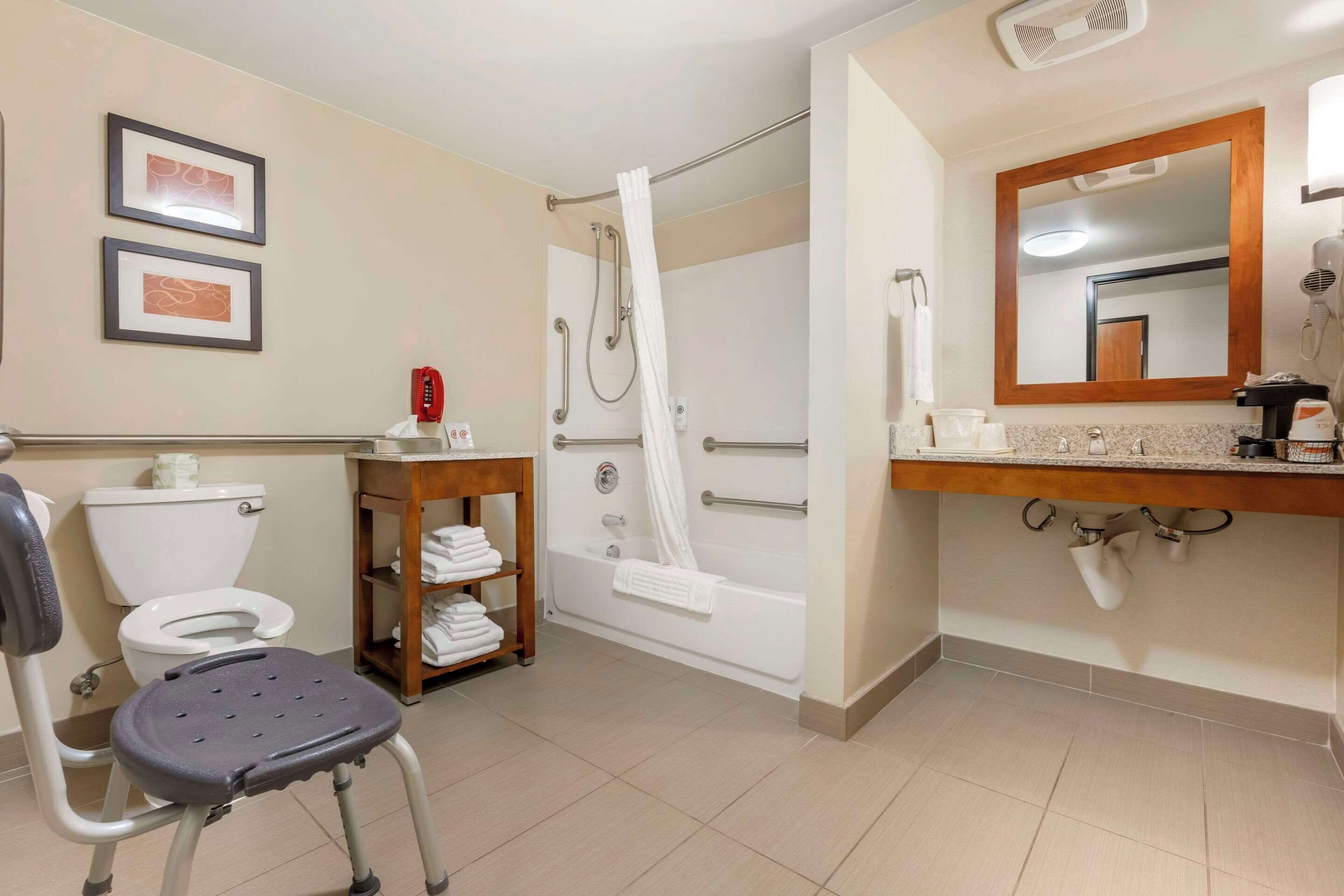 A bathroom with a toilet, shower, and a chair.