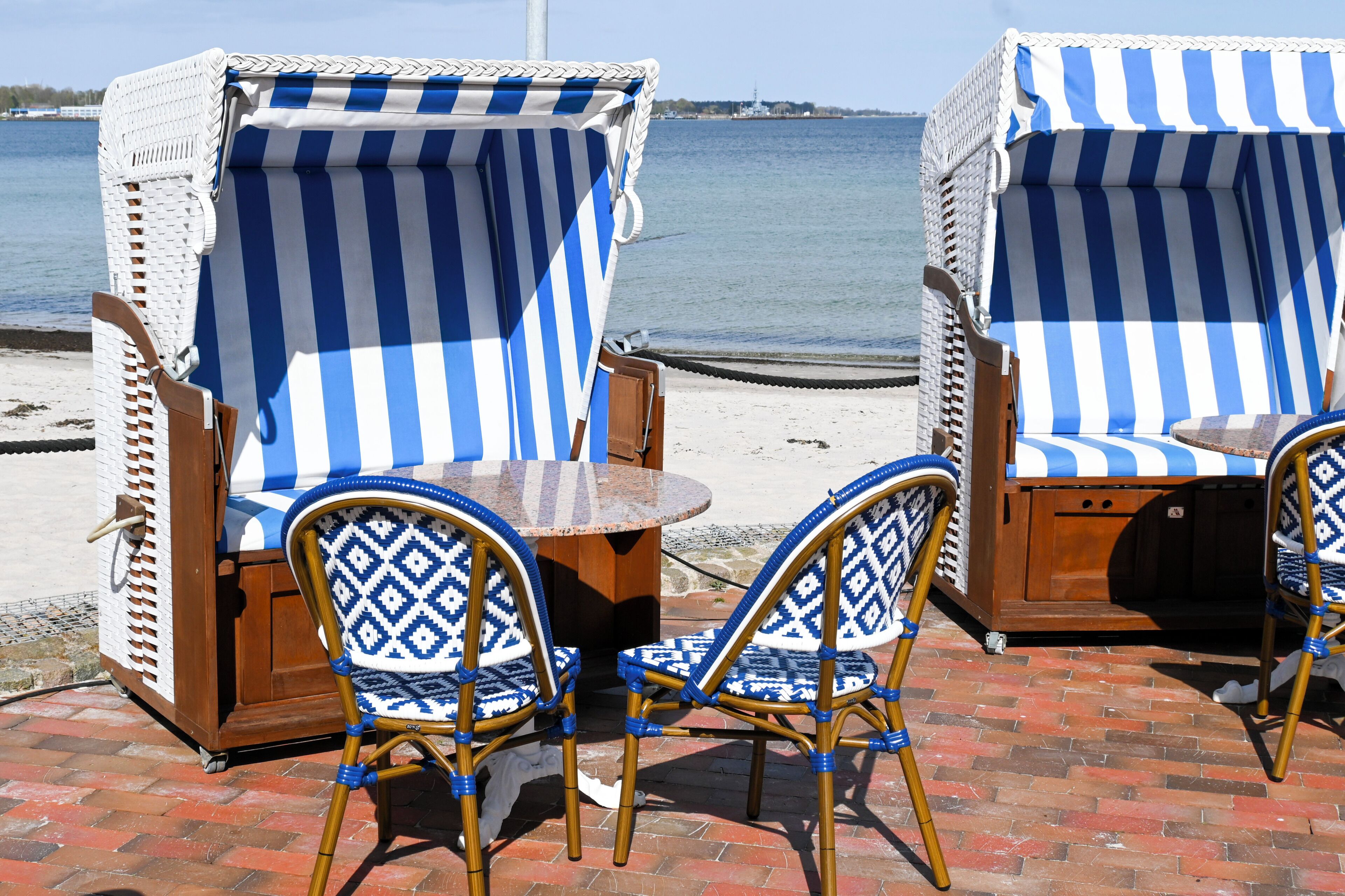 Dos sillas de mimbre con fundas a rayas azules y blancas, una mesa redonda de madera y vistas al mar.