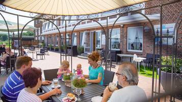 Guests can dine al fresco under a shaded canopy, surrounded by lush greenery and comfortable wicker seating.