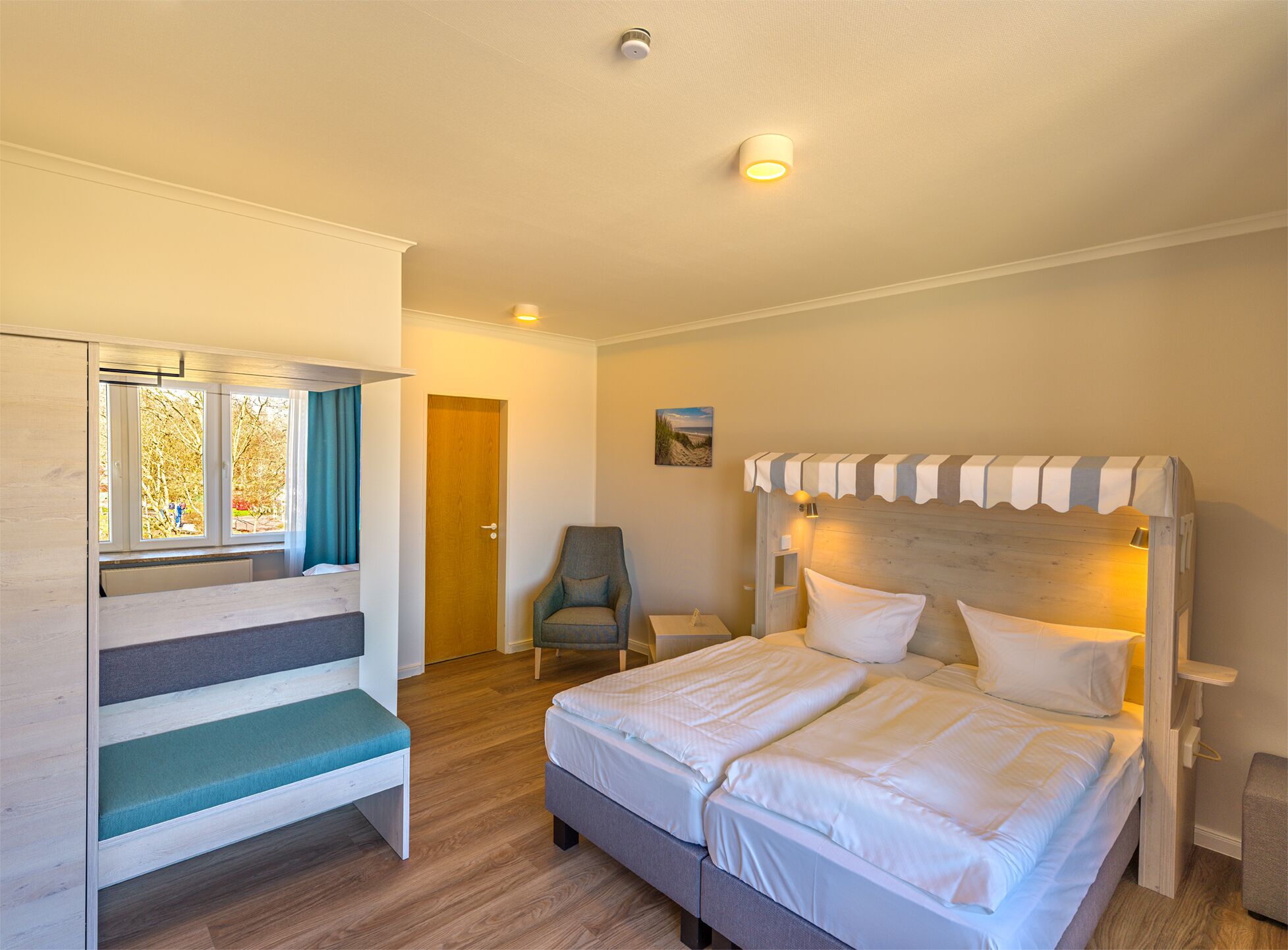 A bedroom with a bed, a chair, a window with curtains, a door, and a small table.