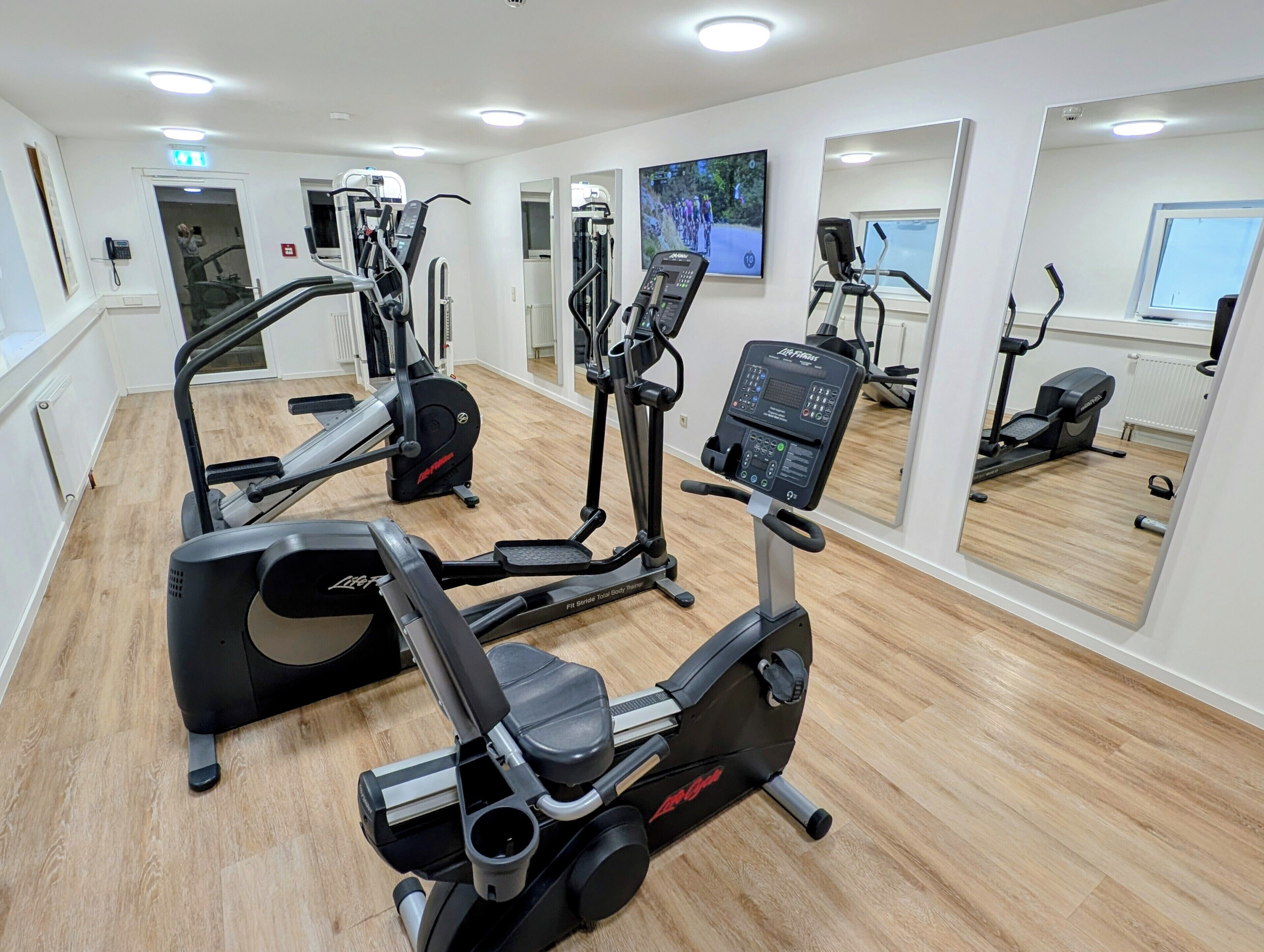 Une salle de sport équipée de divers appareils d’exercice, d’un grand miroir et d’une fenêtre.