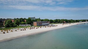Un hôtel situé en bord de mer, avec une plage de sable, un bâtiment portant l’inscription « HÔTEL SEE LUST », et une mer calme.