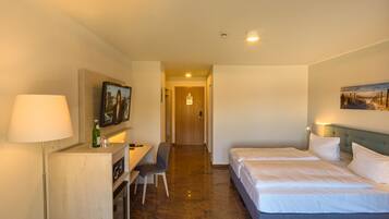 A hotel room with a bed, a desk with a chair, a television, and a painting on the wall.