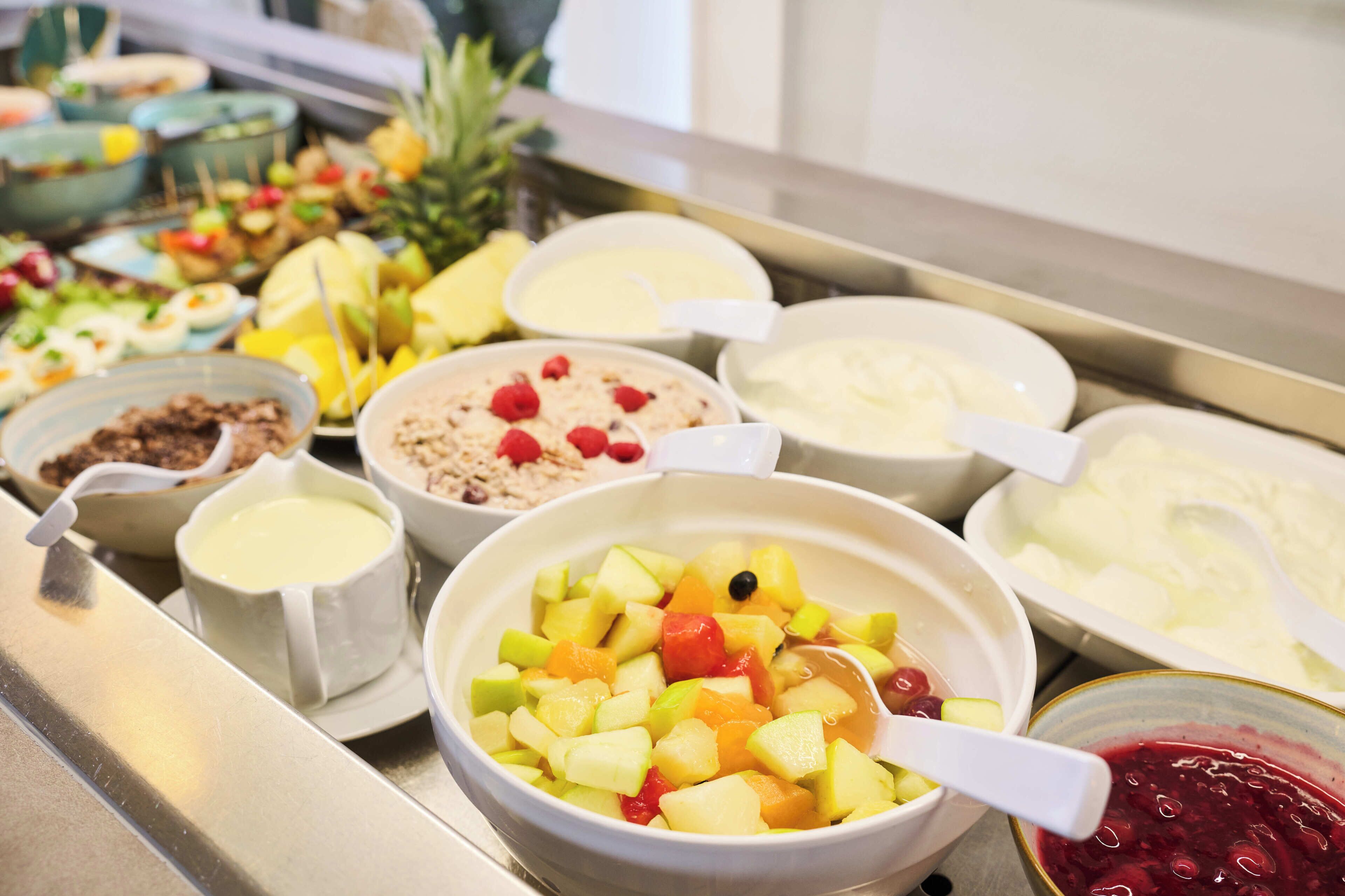Un bufé con diversas opciones de comida, incluyendo frutas, yogur y otros platos.