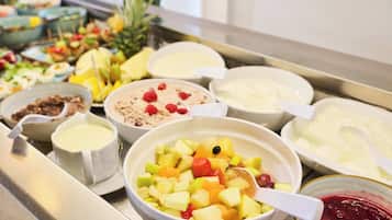 Un bufé con diversas opciones de comida, incluyendo frutas, yogur y otros platos.
