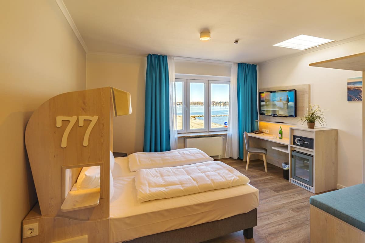 Habitación de hotel con cama, escritorio con computadora, televisor y ventana con vista al mar.