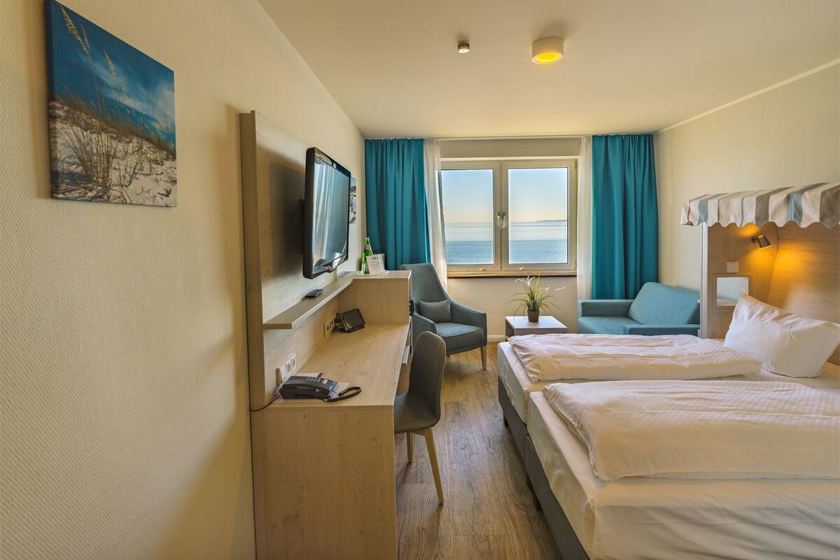 Una habitación de hotel con escritorio, dos camas, televisor y ventana con vistas.