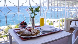 Bandeja de desayuno con pasteles y fruta en un balcón con vistas al mar.