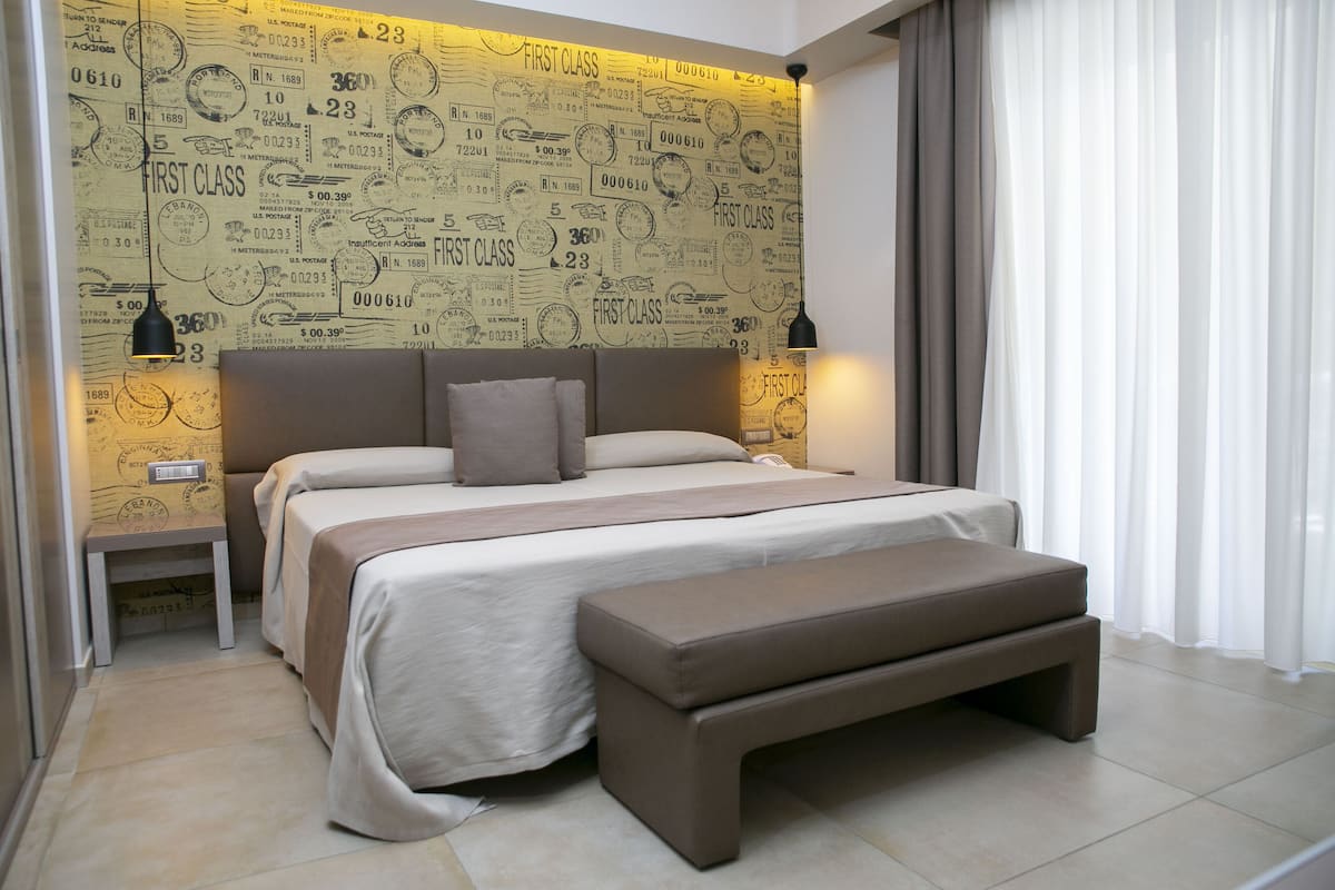 Une chambre moderne avec un grand lit, un banc et un mur décoré de motifs représentant des timbres postaux.