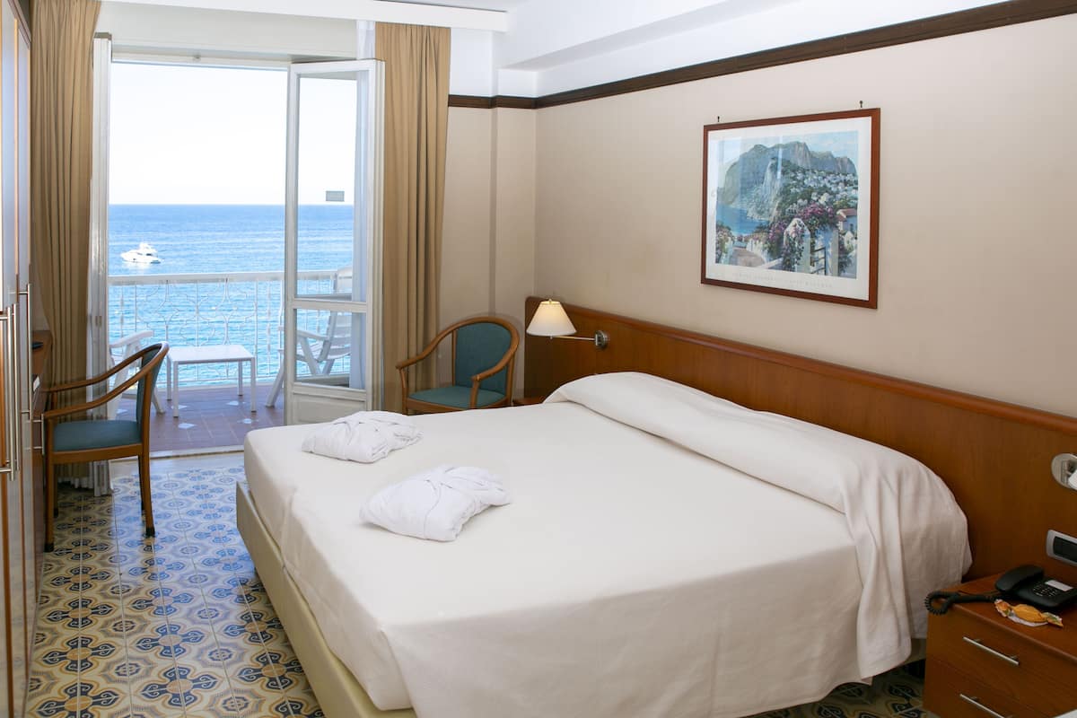 Une chambre d’hôtel avec un lit, une chaise, un bureau et une vue sur la mer.