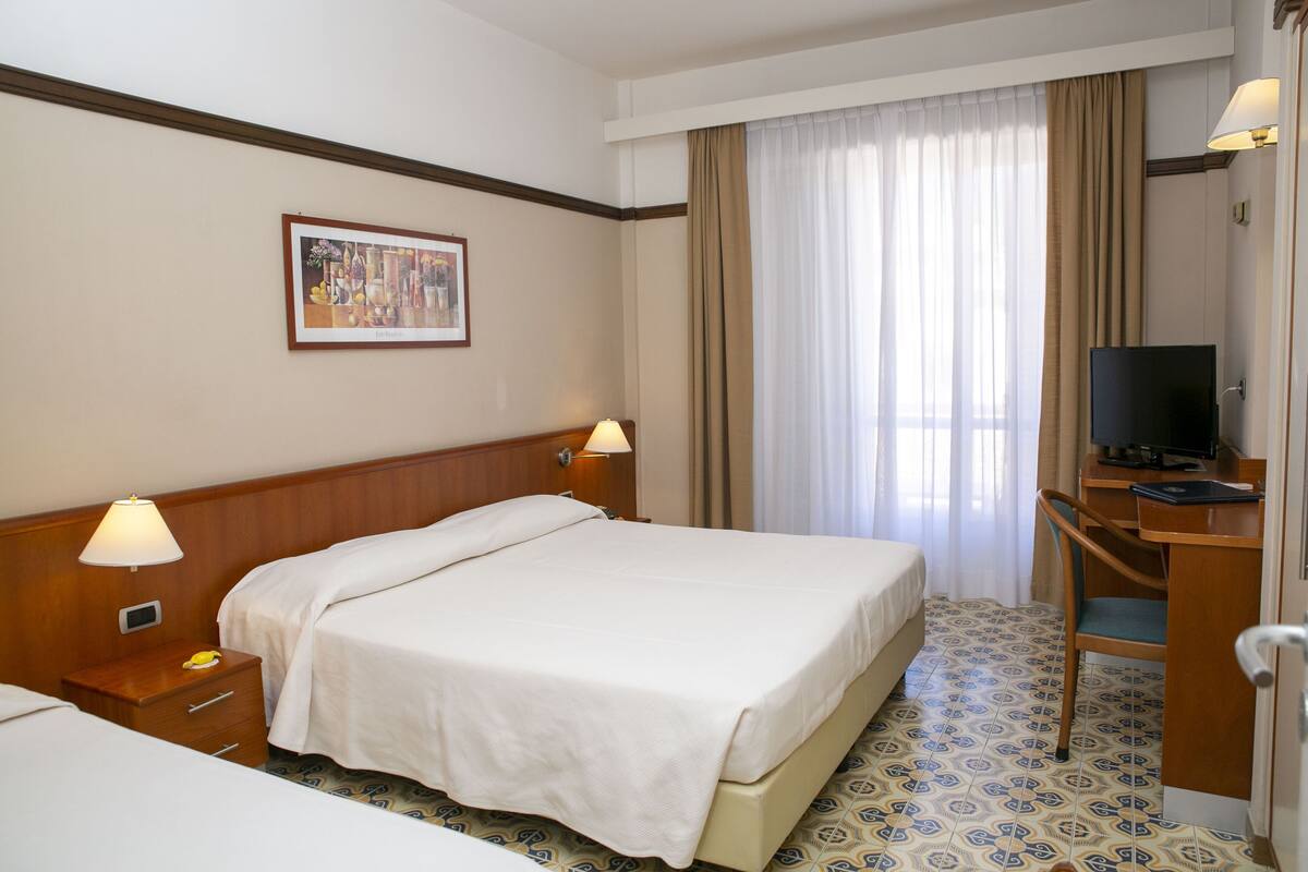 Une chambre d’hôtel avec deux lits, un bureau avec une télévision, une lampe et un tableau au mur.