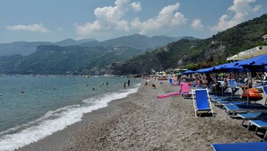 Una playa con orilla pedregosa, sombrillas azules y sillas de descanso.