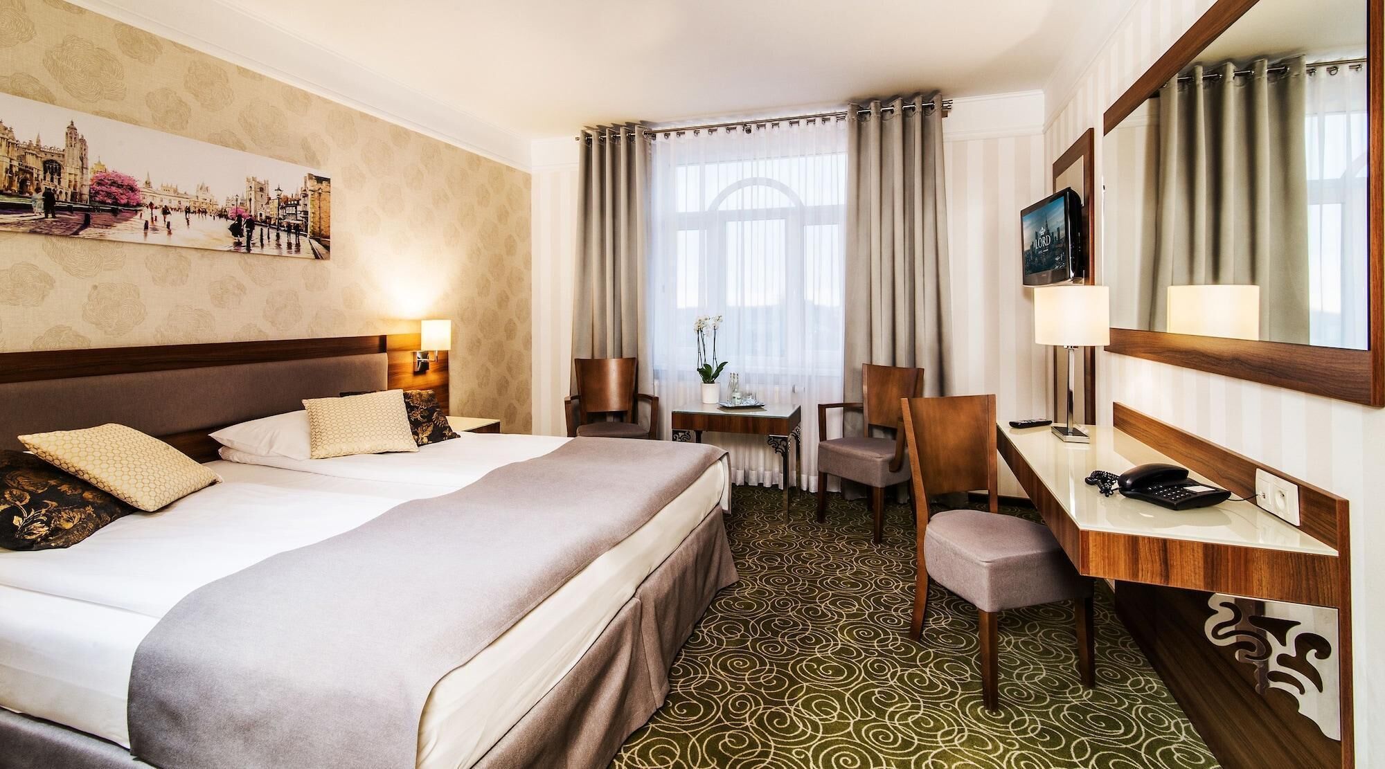 A hotel room with a large bed, a desk with a chair, a television, and a window with curtains.