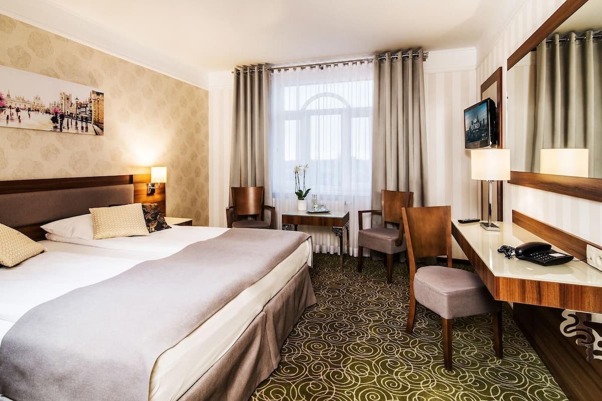 Una habitación de hotel con una cama grande, un escritorio con una silla, un televisor y una ventana con cortinas.