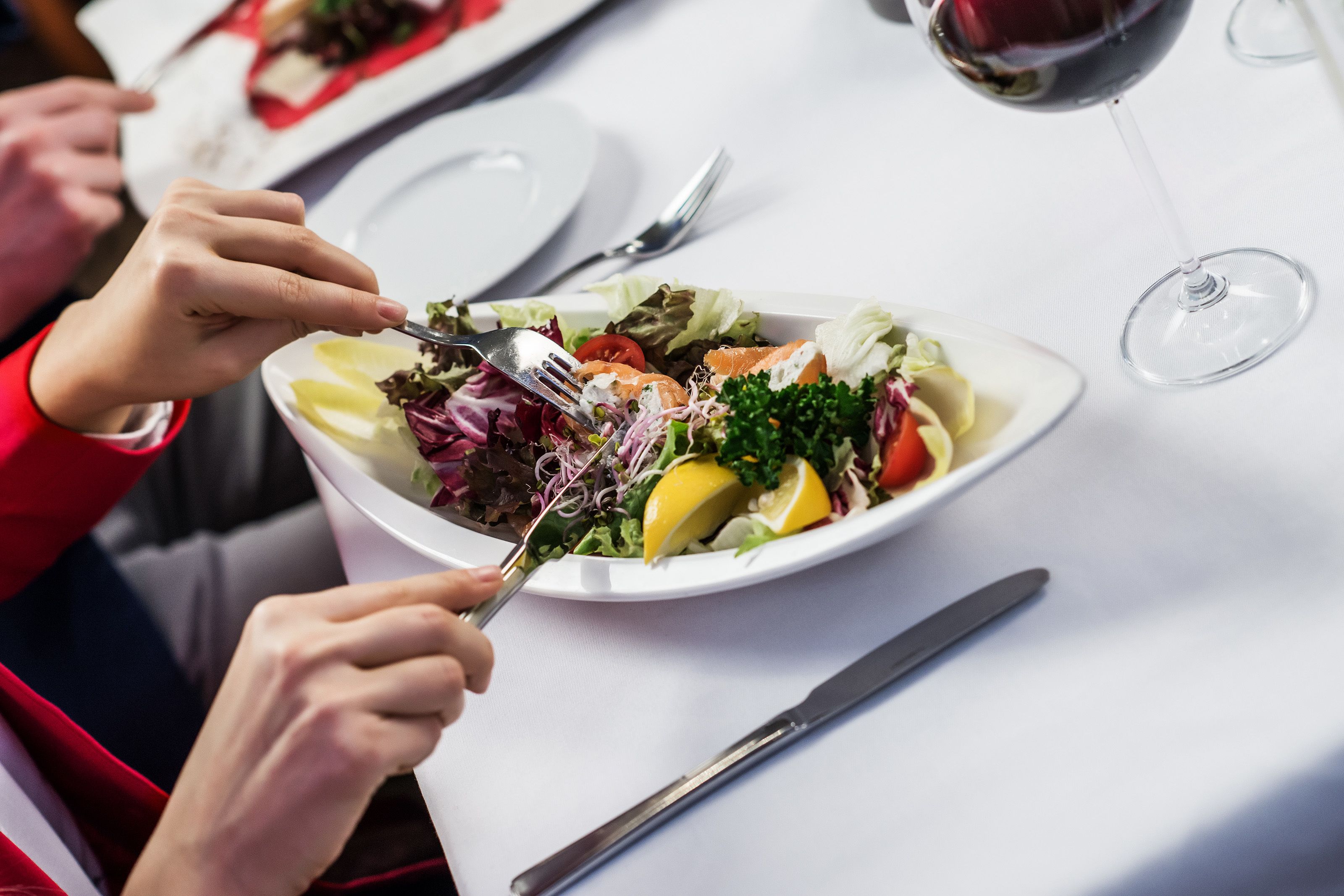 A dining table with a plate of salad and a wine glass.