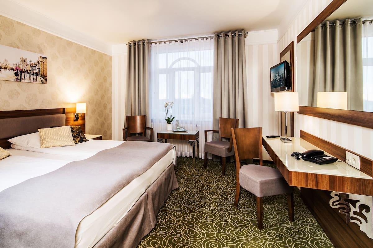 Une chambre d’hôtel avec un grand lit, un bureau avec une chaise, une télévision et une fenêtre avec des rideaux.