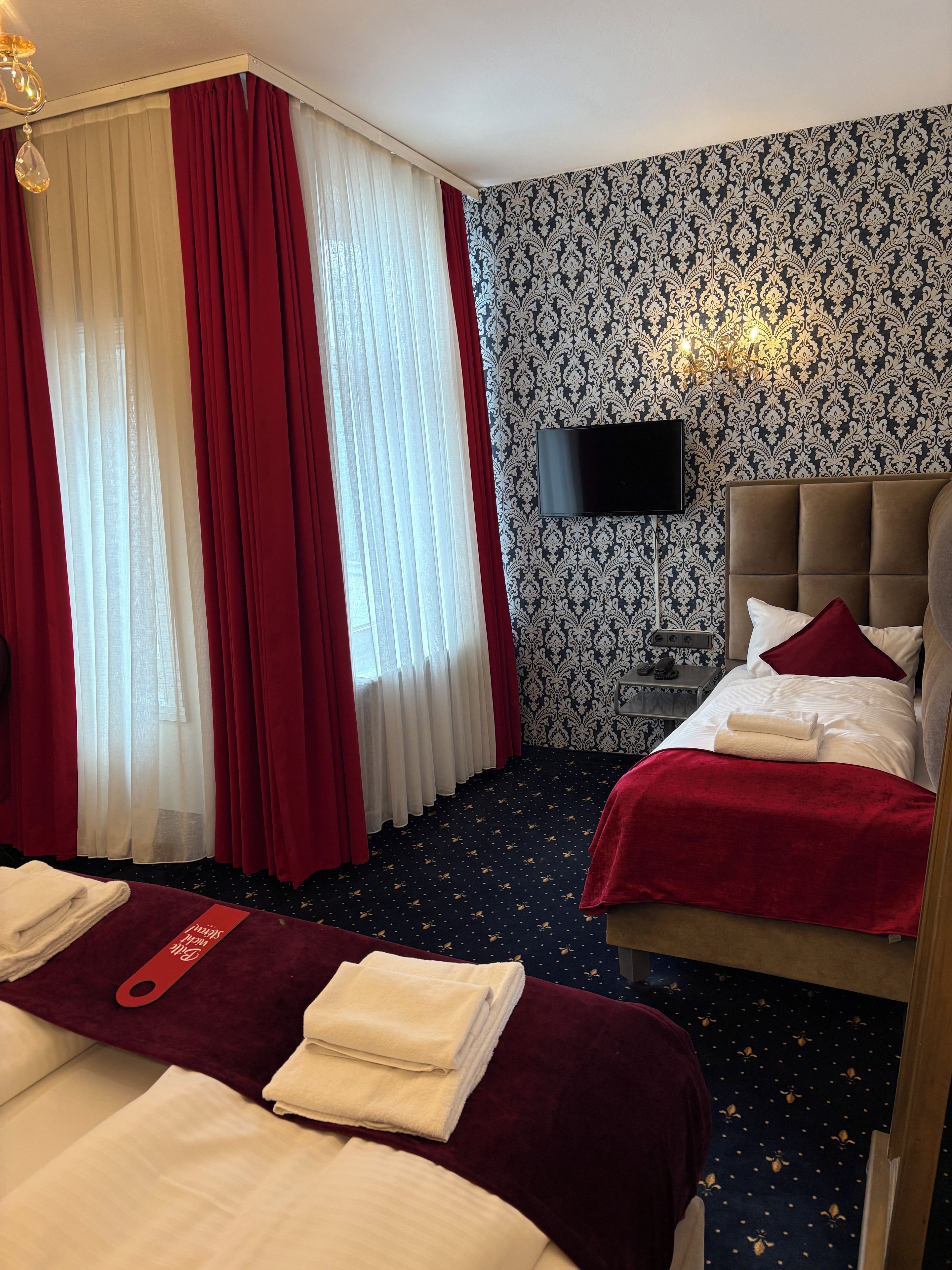 Een hotelkamer met twee bedden, een flatscreen televisie, een nachtkastje en behang met een patroon.