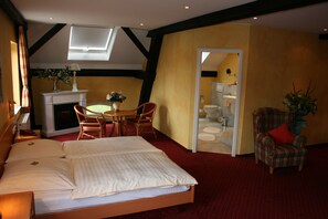 A hotel room with a large bed, a dining area with a table and chairs, a fireplace, and a bathroom visible through an open door. - Hotel Landhaus Knappmann (Essen)