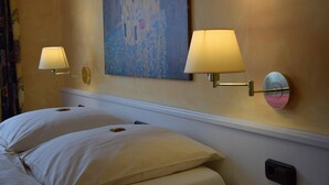 Quarto de hotel com duas camas, um quadro na parede e luminárias fixadas na parede.
