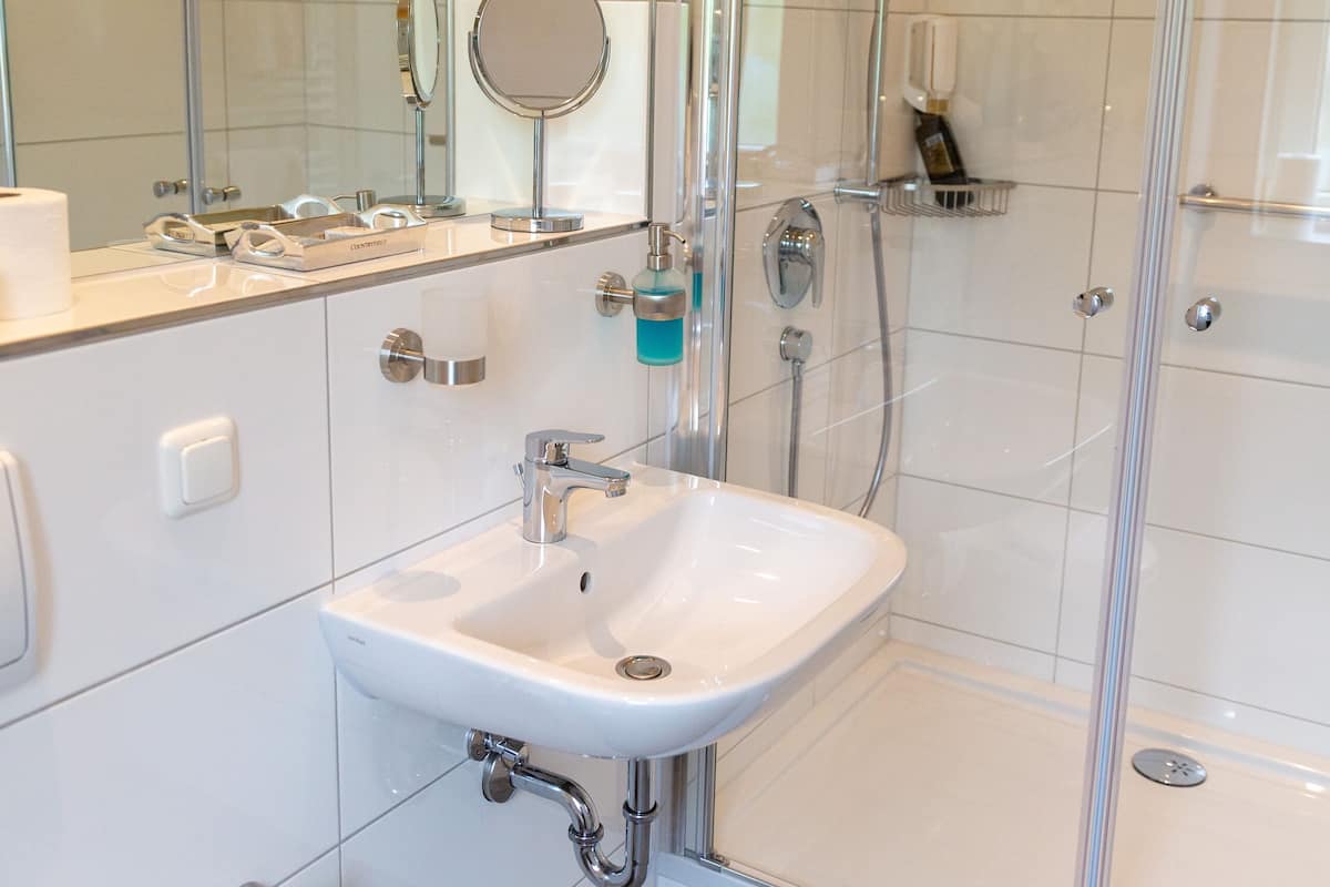 A modern bathroom with a glass-enclosed shower, a white sink, and a mirror above it.