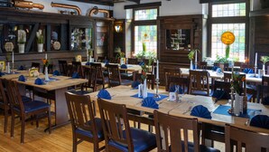 Restaurante com mesas e cadeiras de madeira, janelas com vitrais e um bar com tubos de cobre.