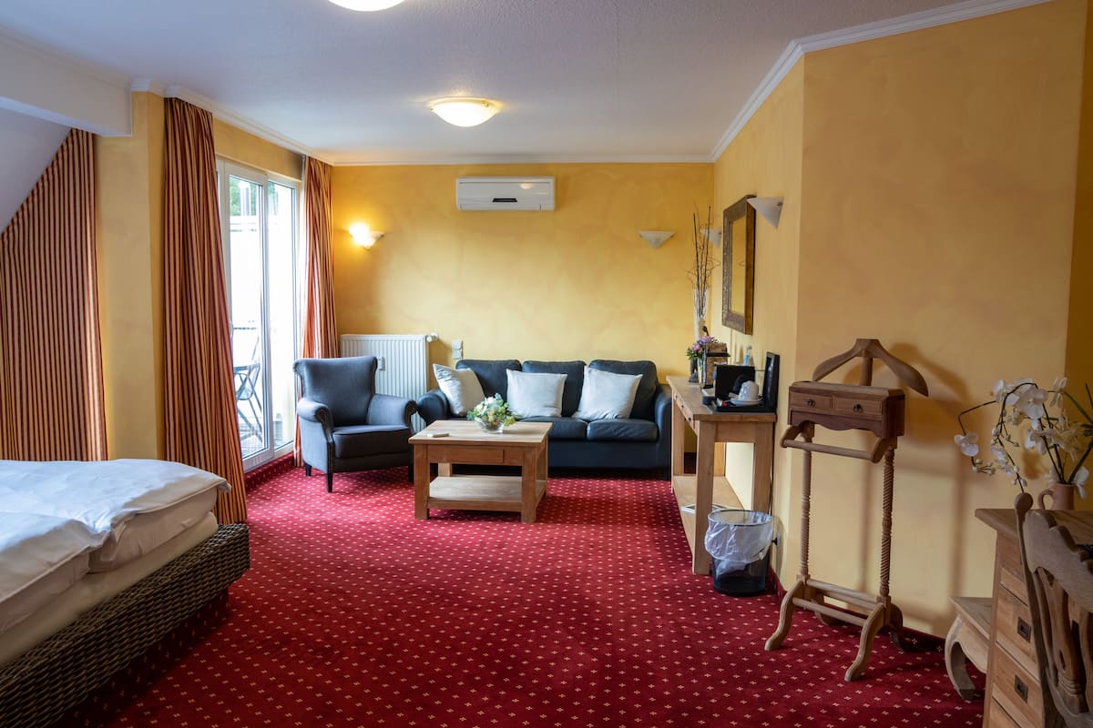 A hotel room with a red carpet, a sofa, a chair, a small table, a dresser, and a window with curtains.