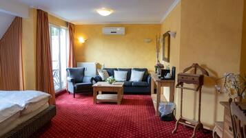A hotel room with a red carpet, a sofa, a chair, a small table, a dresser, and a window with curtains.