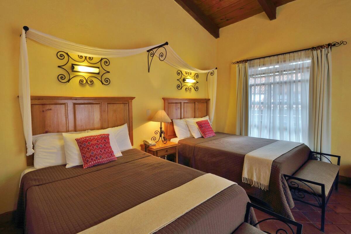 A hotel room with two beds, a small table, and a chair.