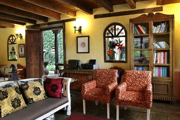 Una sala de estar acogedora con un banco de madera, dos sillones estampados, una estantería y un escritorio con un ordenador portátil.