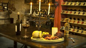 Una mesa de madera con una botella de vino, una copa de vino, un queso redondo, uvas y diversos tipos de carne.