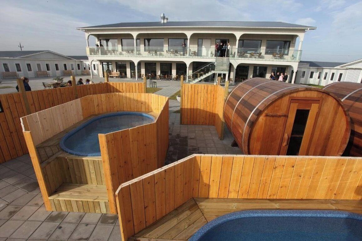 Een houten terras met een jacuzzi en houten vaten, en een gebouw met balkons op de achtergrond.