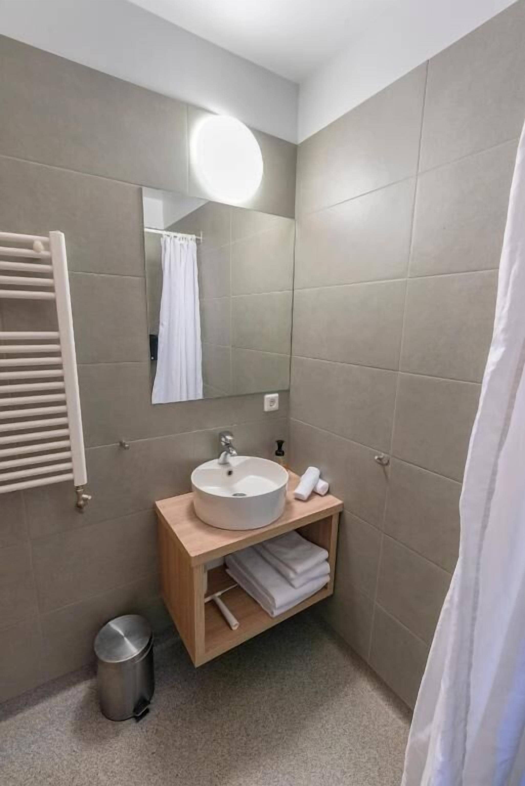 A bathroom with a sink, mirror, towel rack, and a trash bin.