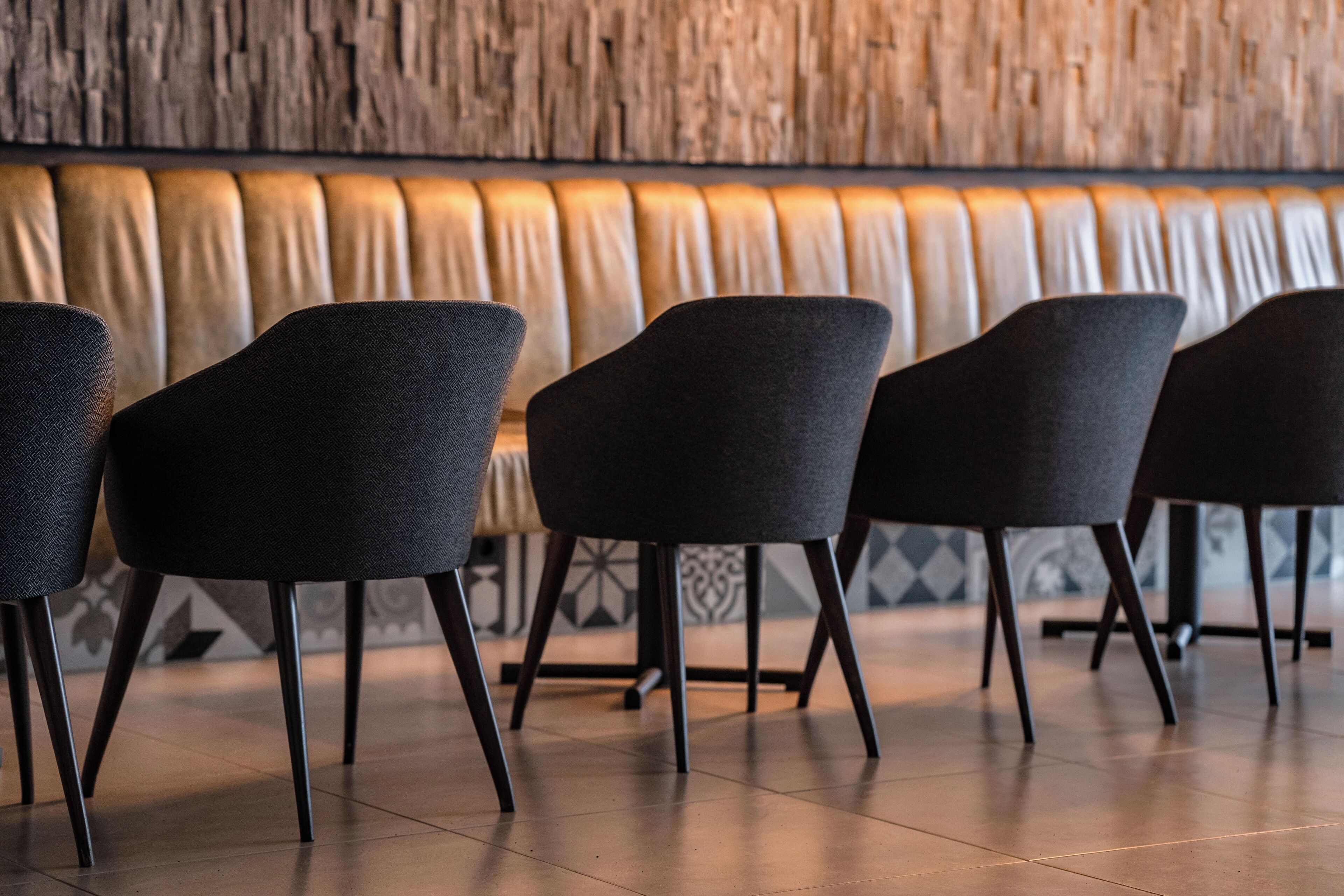 A row of modern chairs with a wooden wall and patterned floor tiles in the background.