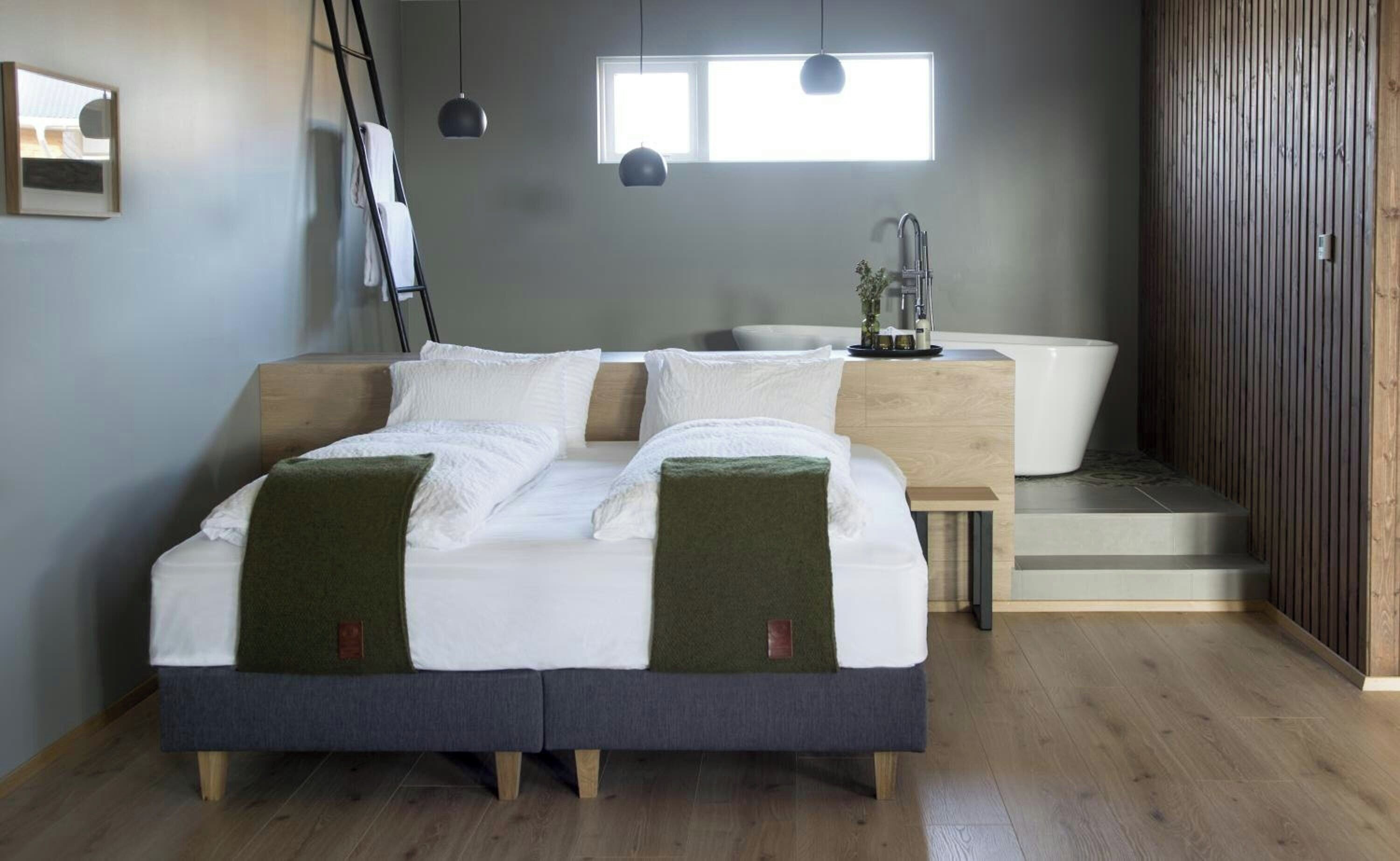 A bedroom with a bed, a bedside table, a window, and a bathroom with a bathtub.
