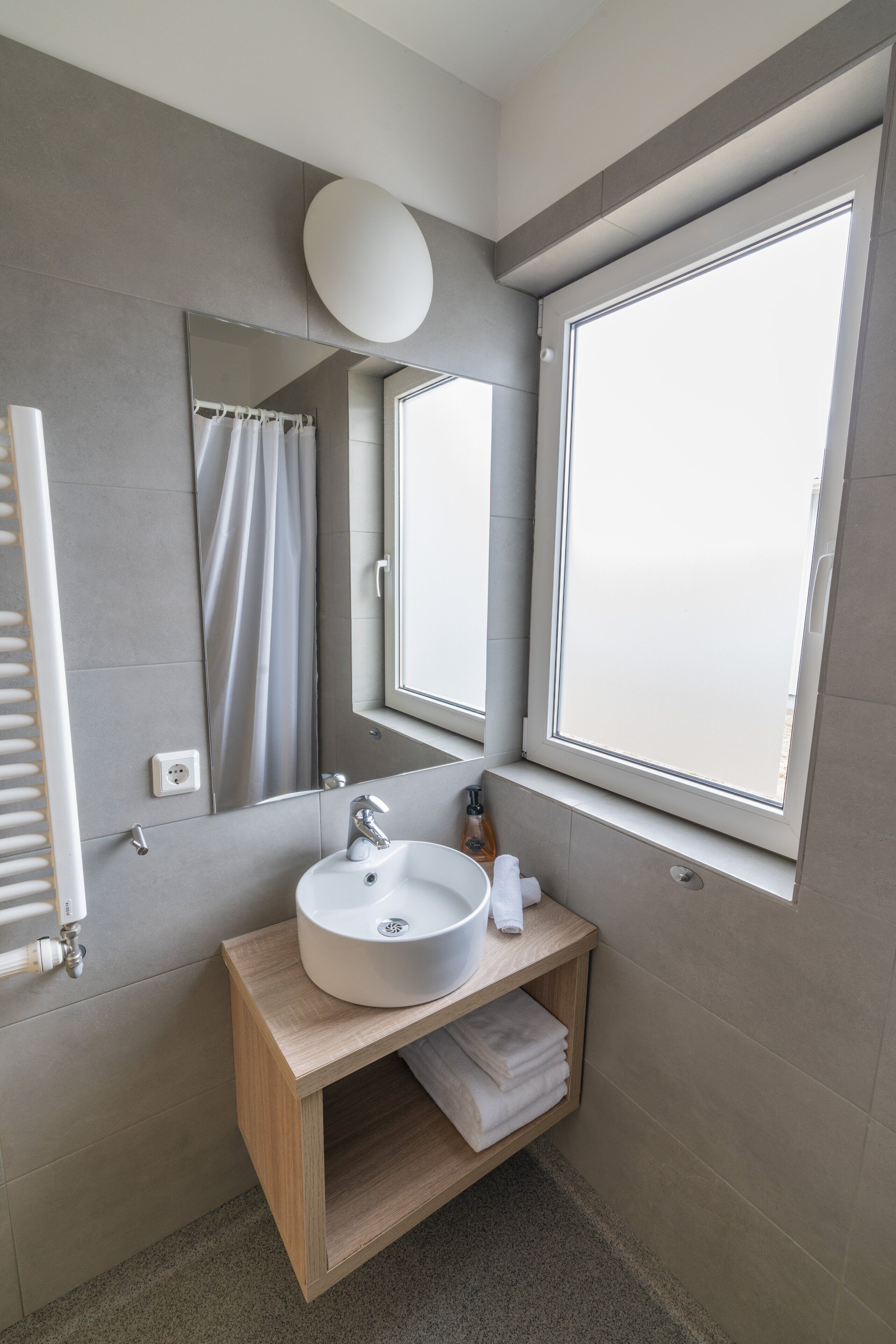 A modern bathroom with a large mirror, a window, and a wooden vanity.
