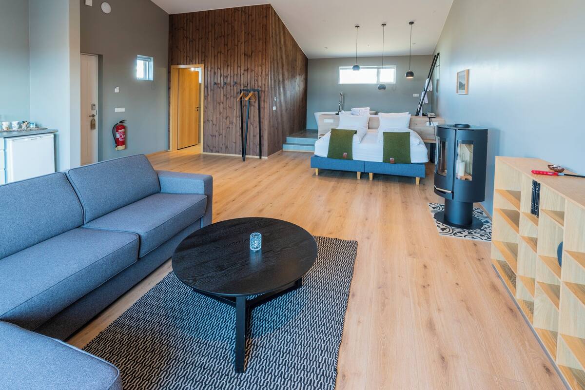 A modern living room with a sofa, a coffee table, a fireplace, and a staircase leading to a bedroom.